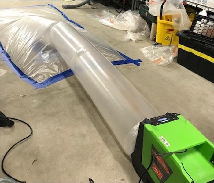 Dehumidifier connected to plastic sheeting drying a water damaged floor